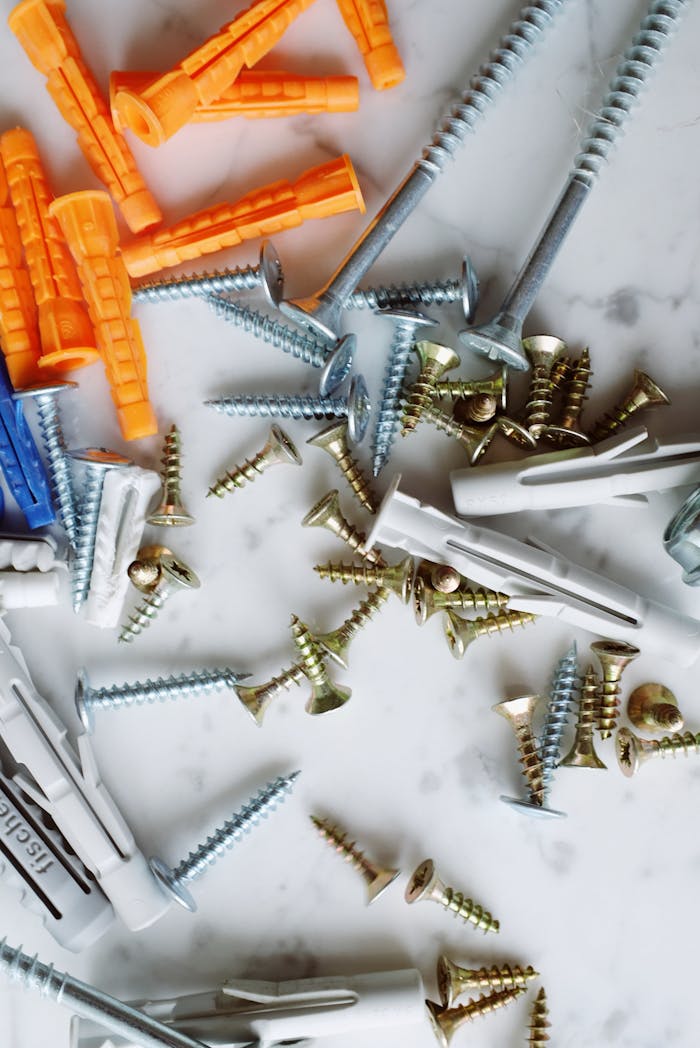Set of various multicolored plastic dowels with metal screws of different sizes placed on white marble table in modern workshop